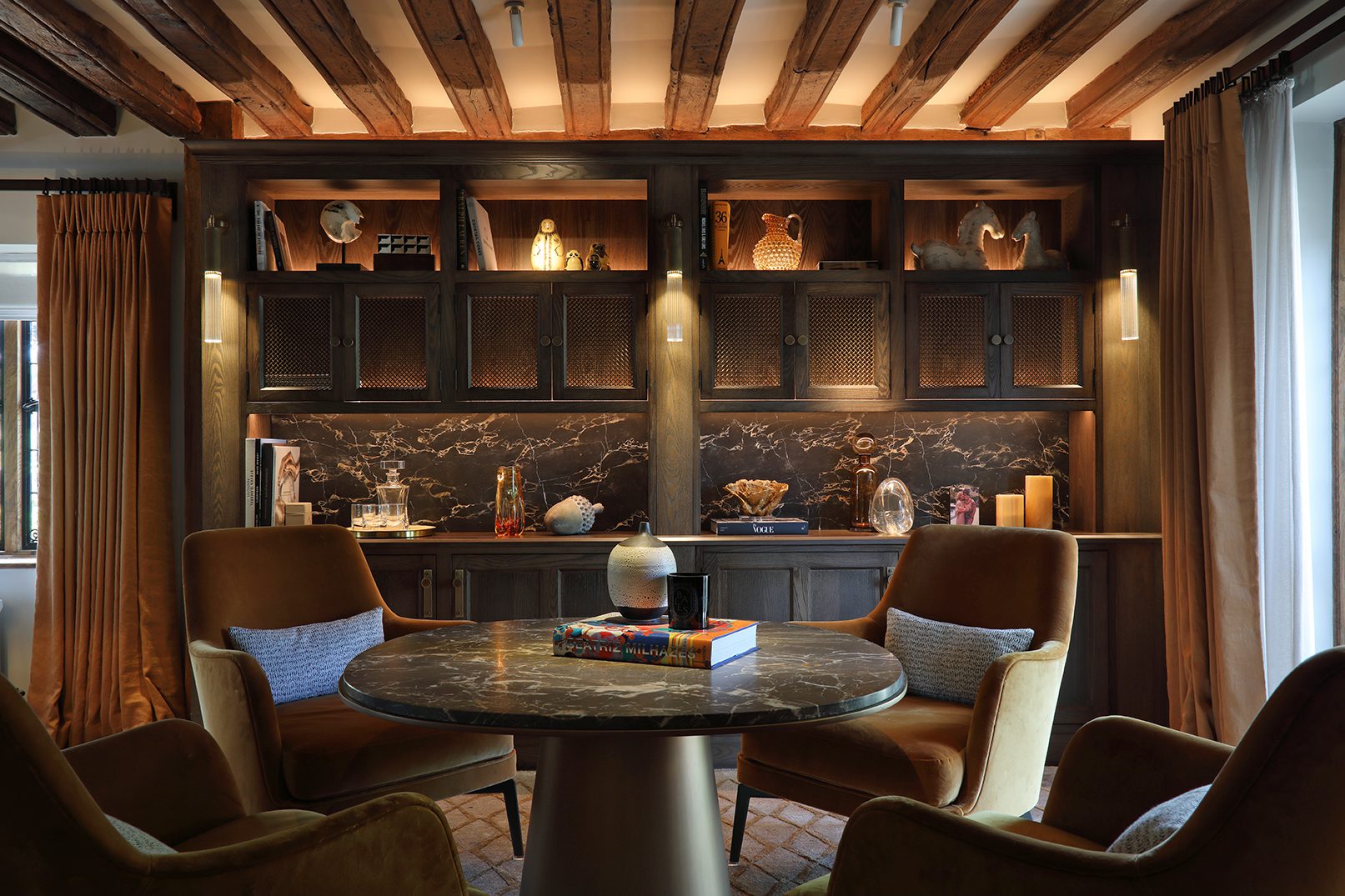 Dark oak display cabinetry with marble backsplash and lit display shelves, exposed beam ceiling and round marble table