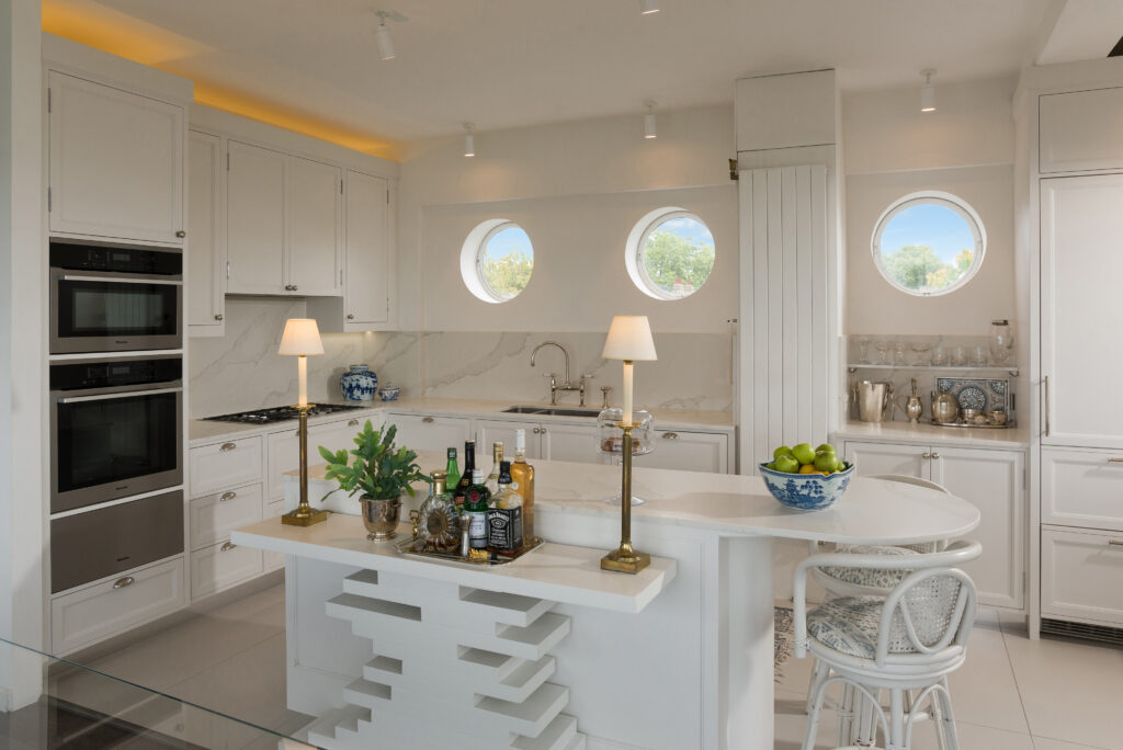 White panelled kitchen nook with round porthole window, open display shelving and integrated tall fridge freezer