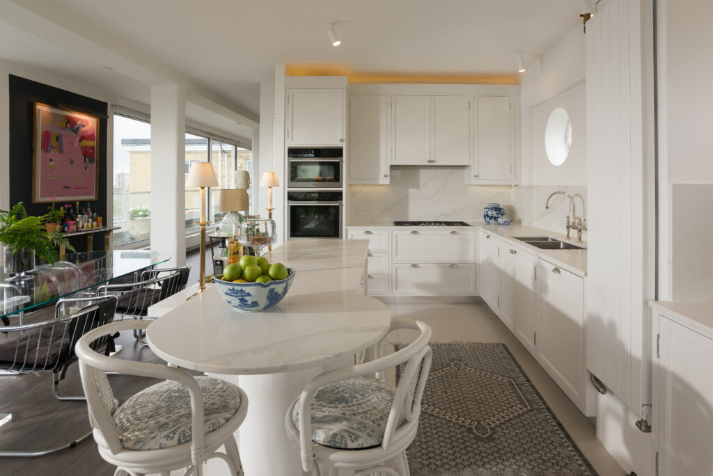 White panelled kitchen nook with round porthole window, open display shelving and integrated tall fridge freezer
