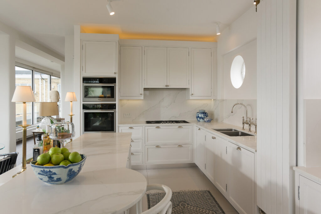 White panelled kitchen nook with round porthole window, open display shelving and integrated tall fridge freezer
