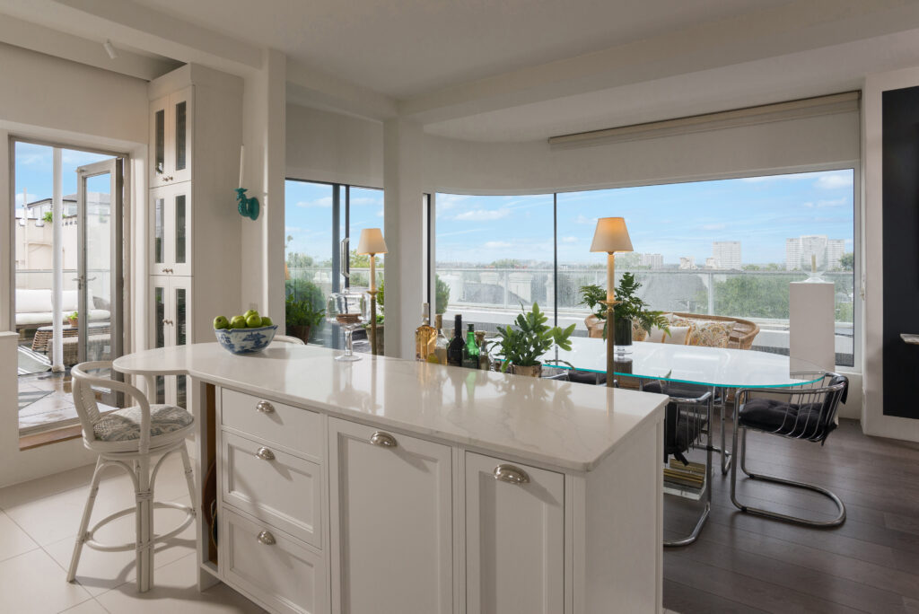 White panelled kitchen nook with round porthole window, open display shelving and integrated tall fridge freezer