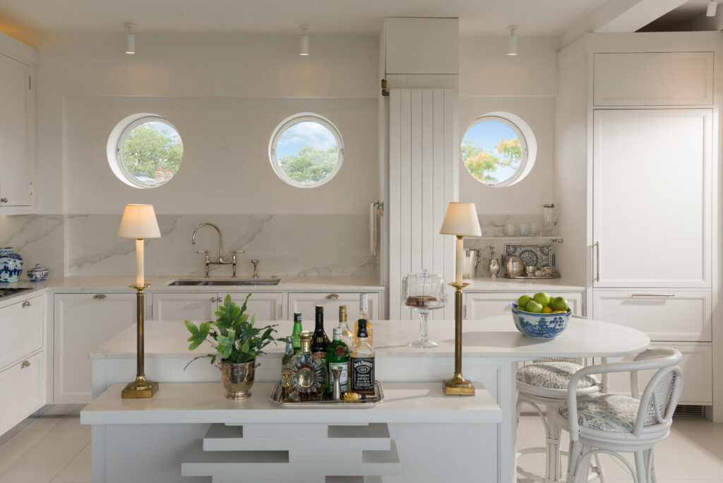 White panelled kitchen nook with round porthole window, open display shelving and integrated tall fridge freezer