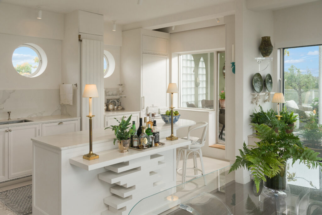 White panelled kitchen nook with round porthole window, open display shelving and integrated tall fridge freezer
