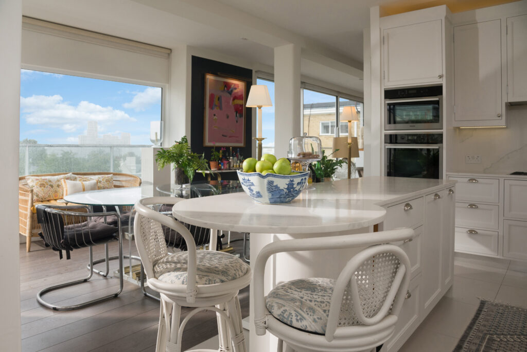White panelled kitchen nook with round porthole window, open display shelving and integrated tall fridge freezer