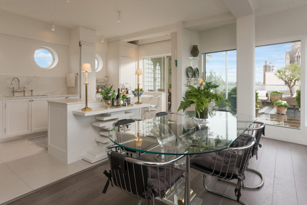 White panelled kitchen nook with round porthole window, open display shelving and integrated tall fridge freezer