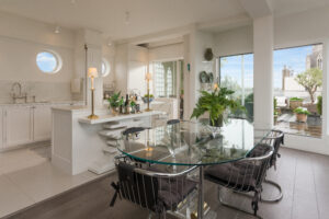 White panelled kitchen nook with round porthole window, open display shelving and integrated tall fridge freezer