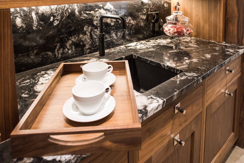 Close-up of a dark stone kitchen sink and marble worktop, with a wooden chopping surface